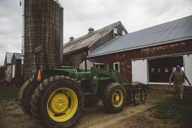 Green John Deere tractor parked near barn and silo on rural farm