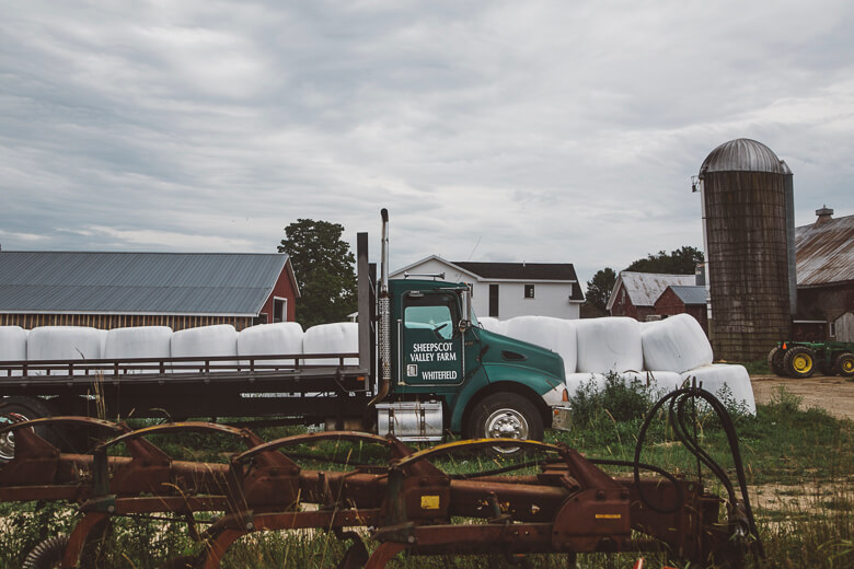Green truck with hay bales on farm with red barn and silo
