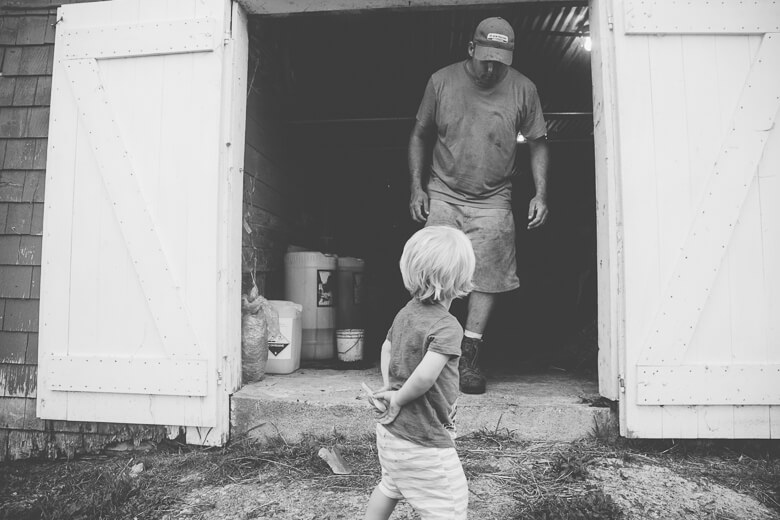 Child watching adult in shed doorway, black and white candid moment