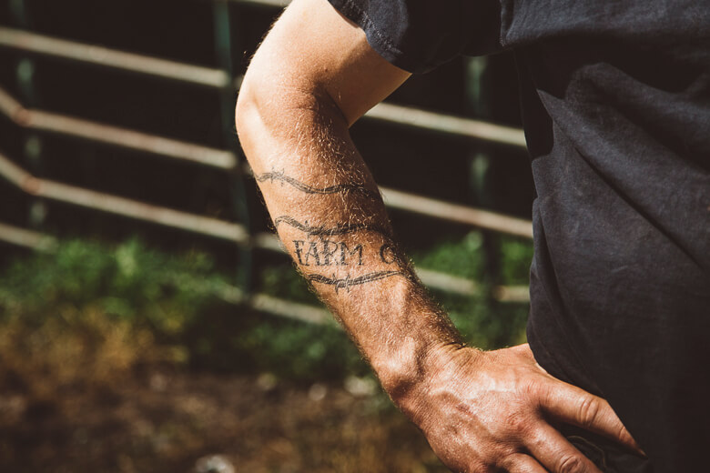 Muscular arm with farm tattoo against blurry wooden fence background