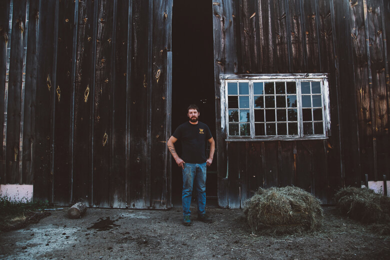 Person standing in front of weathered wooden barn with hay bales