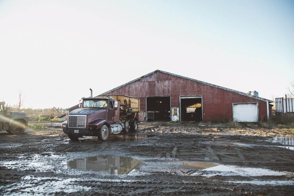 Red barn and semi-truck on muddy farmyard with puddles and overcast sky