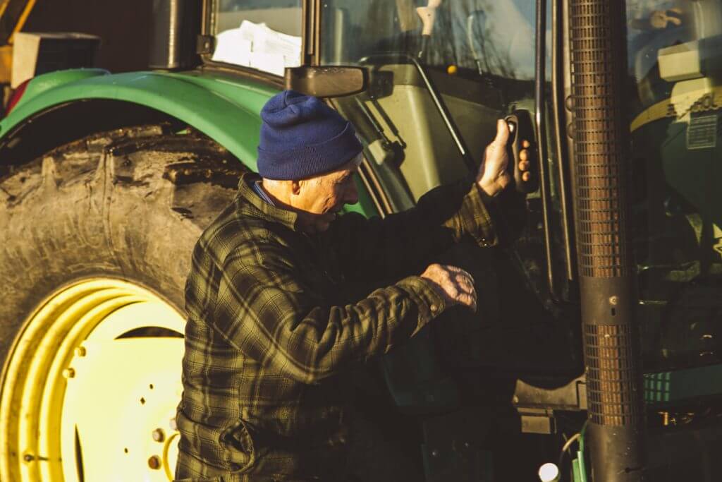 Farmer in blue beanie operating green tractor at golden hour