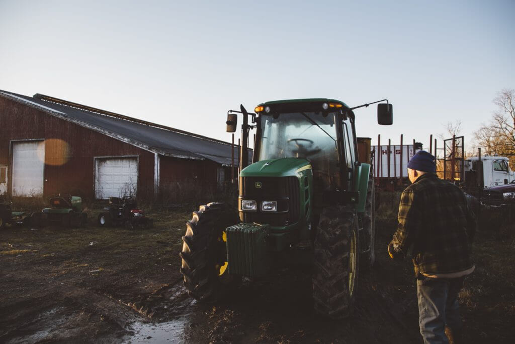 Green John Deere tractor parked near barn with farmer in background