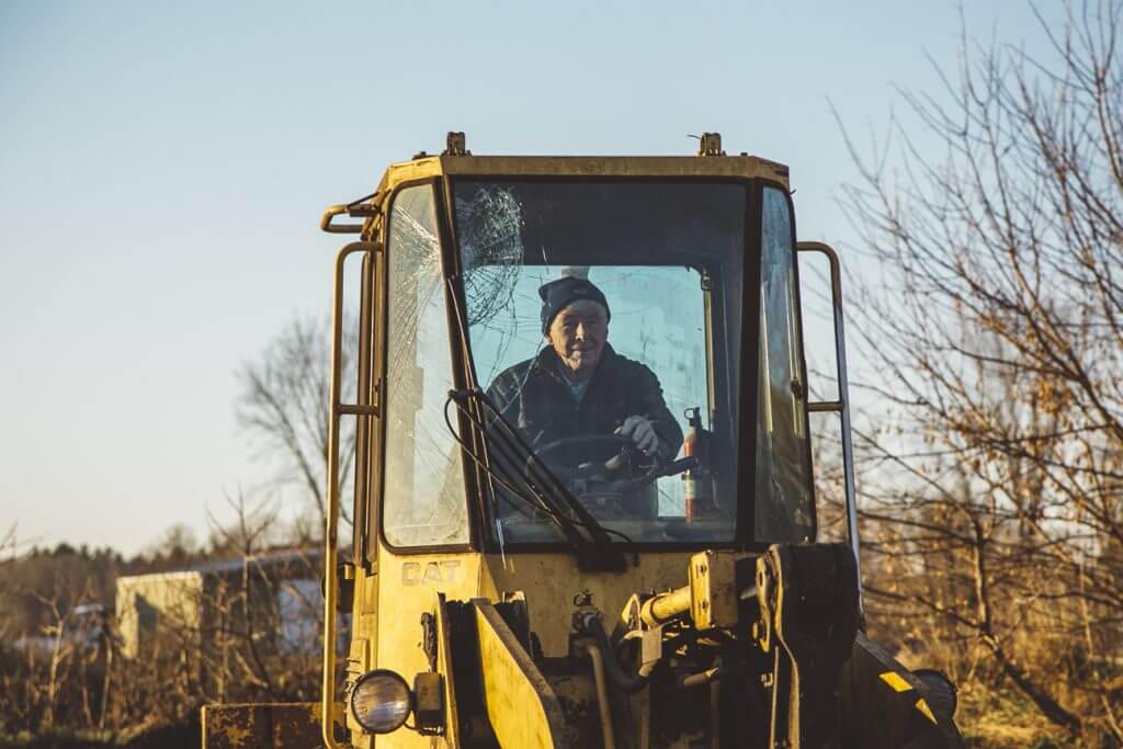 Elderly worker sitting in yellow construction vehicle with cracked windshield