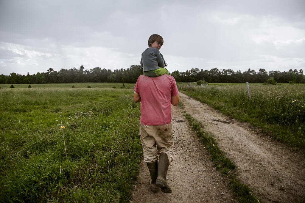 Child sitting on parent's shoulders walking down rural dirt path