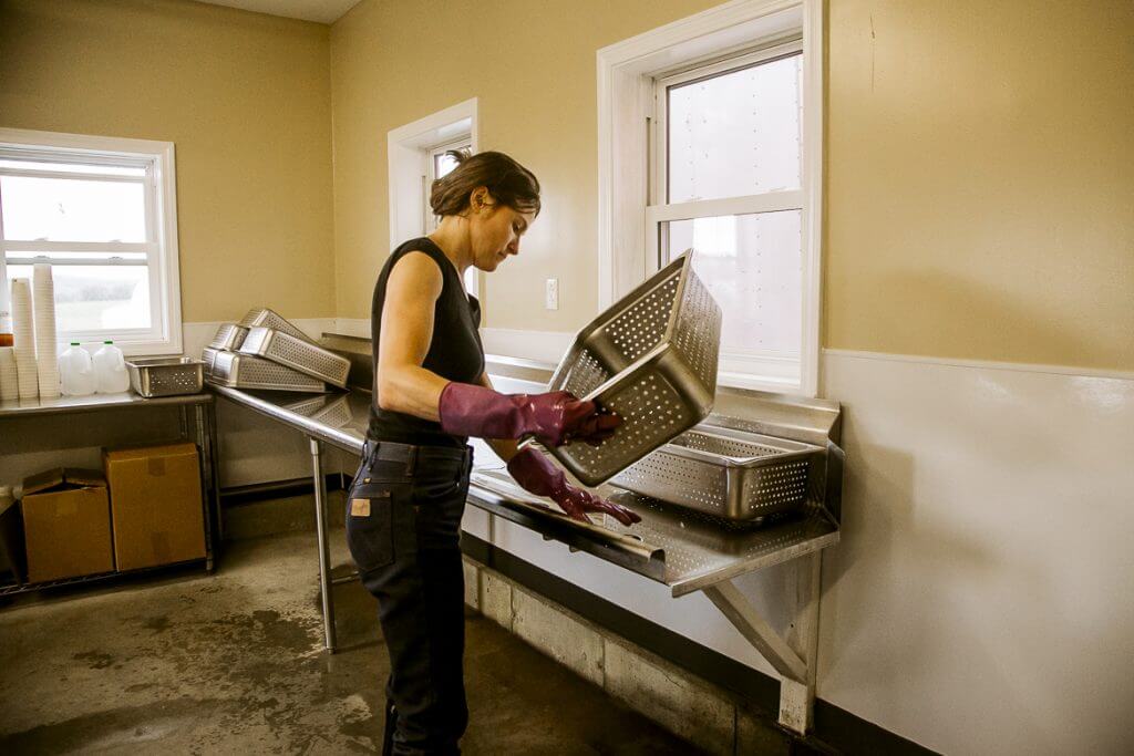 Worker in kitchen wearing gloves handling large metal perforated containers
