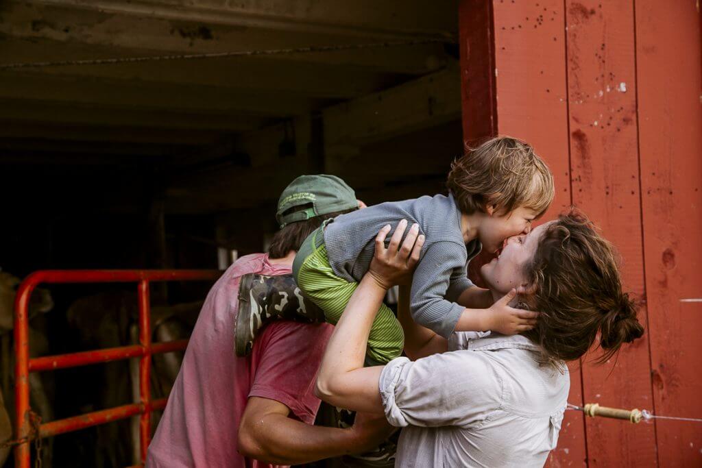 Parent lovingly kisses child in front of rustic red barn door