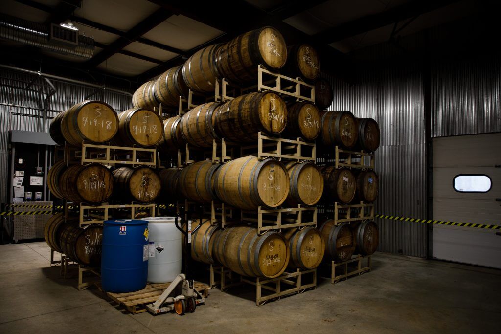Wooden whiskey barrels stacked in rows inside a metal warehouse