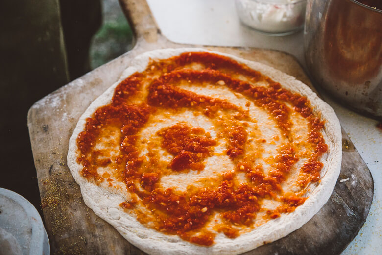 Unbaked pizza dough with red tomato sauce spread in circular pattern