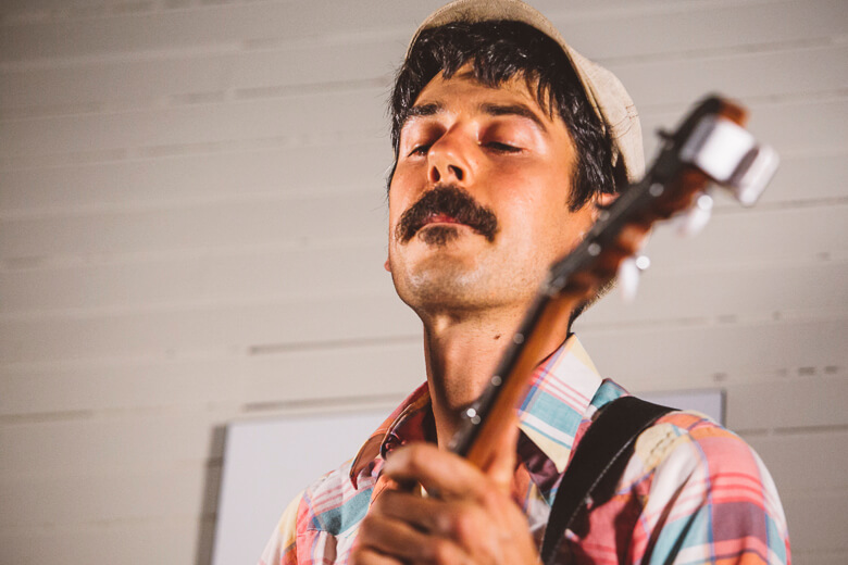 Musician with closed eyes playing guitar in plaid shirt and white hat