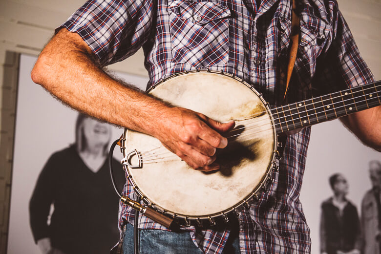 Musician playing vintage banjo in plaid shirt against blurry background