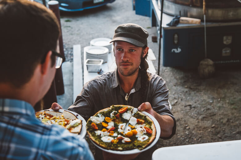 Chef in cap serves colorful vegetable pizza at outdoor kitchen