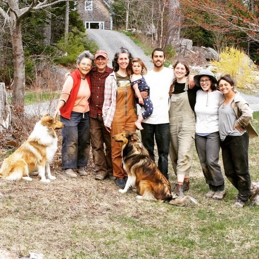 Large family group photo with two dogs outdoors near a country house