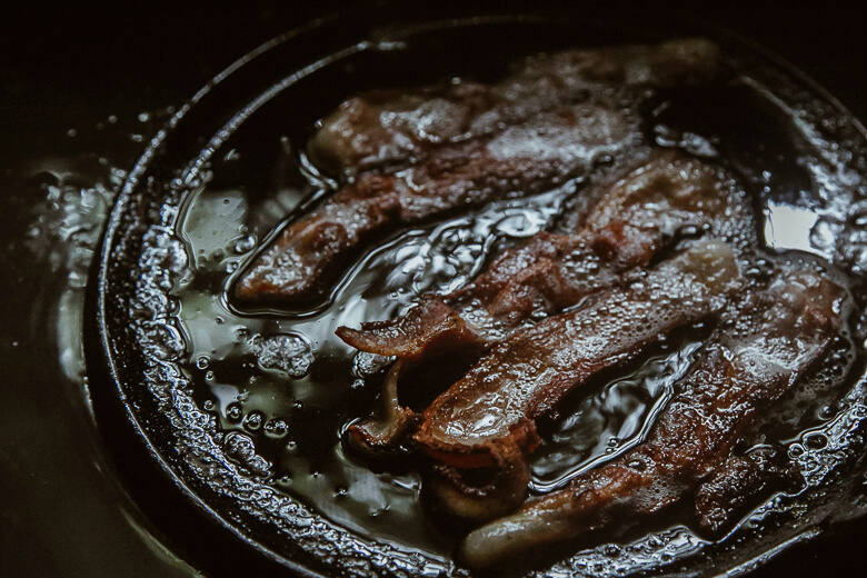 Crispy bacon strips sizzling in a cast iron skillet with bubbling grease