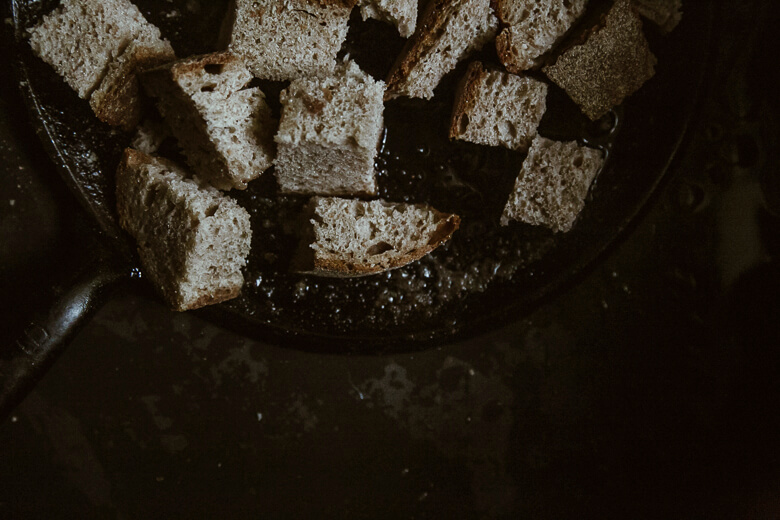 Rustic bread cubes on a dark, textured surface in moody lighting