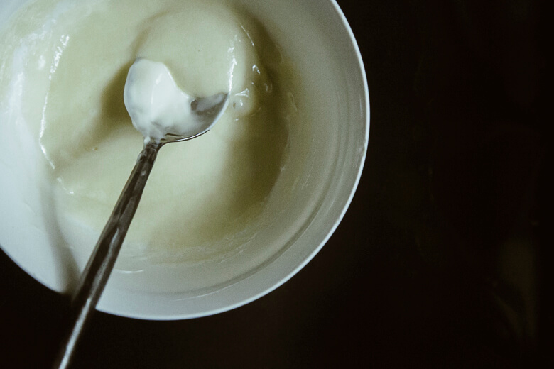 Spoon lifting creamy white yogurt or sour cream from ceramic bowl