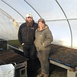 Two farmers standing in greenhouse with seedling trays and white bucket