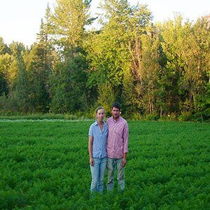 Two people standing together in lush green field with forest background