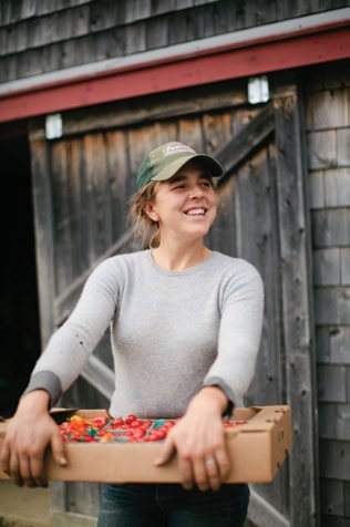 Smiling farmer holding wooden box of fresh red tomatoes