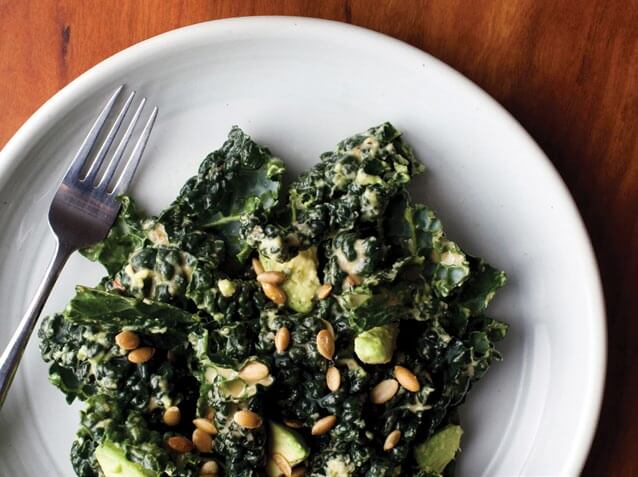 Kale salad with avocado, pine nuts, and creamy dressing on white plate