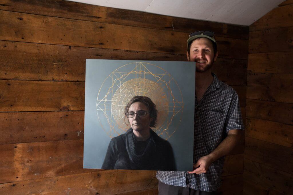 Artist holding portrait with golden geometric pattern behind subject
