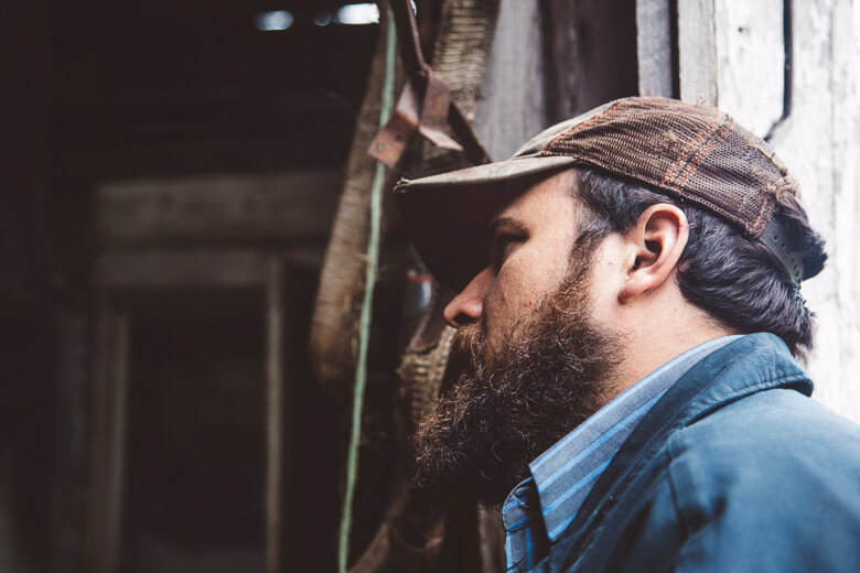 Bearded man in cap looks pensively out wooden window