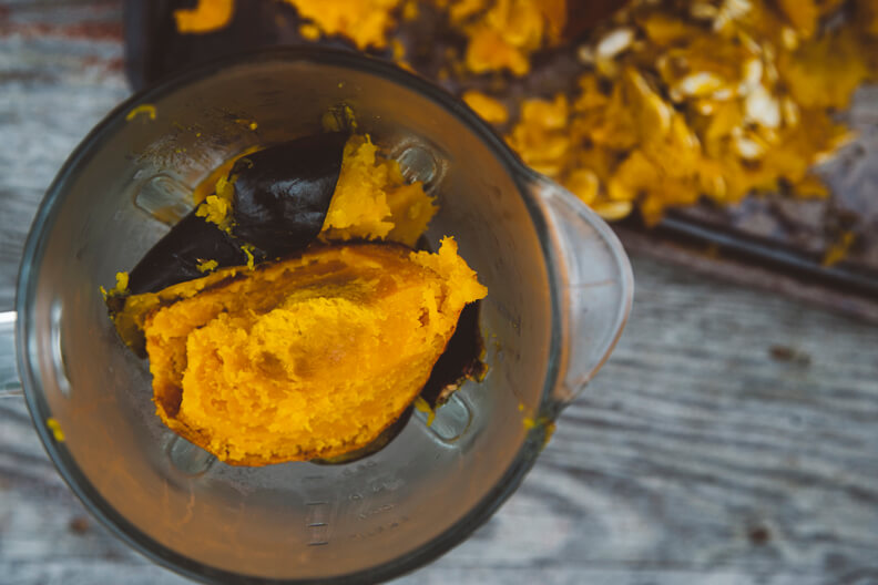 Bright yellow pumpkin puree in a clear blender with scattered pieces around