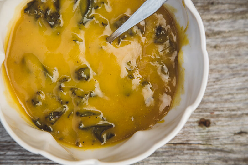 Yellow soup with herbs in a white bowl on rustic wooden surface