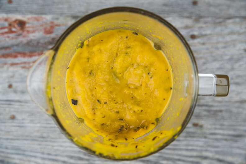Yellow sauce or dressing blended in a glass container with herbs