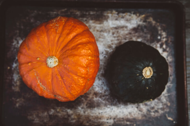 Orange and black pumpkins on rustic baking sheet with textured background