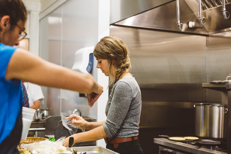 Woman preparing food in commercial kitchen with another person nearby