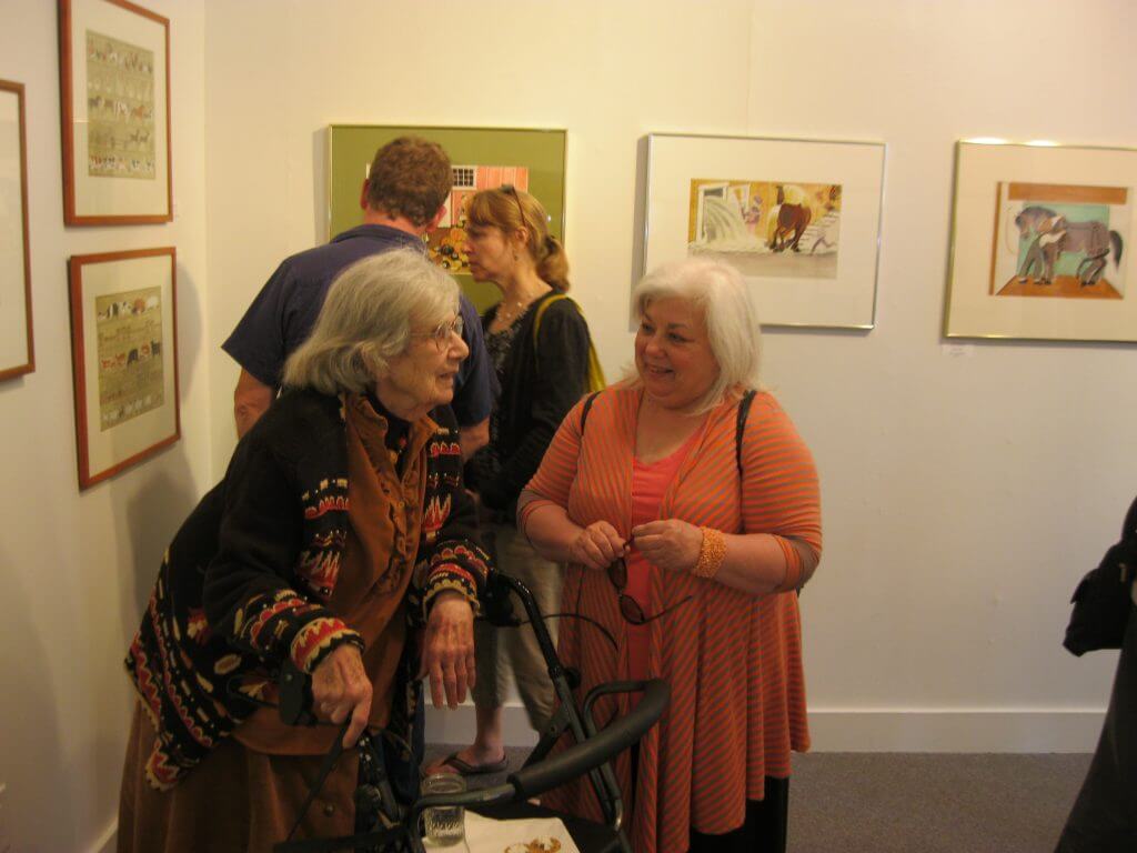 Art gallery visitors chatting near colorful framed artwork on white walls
