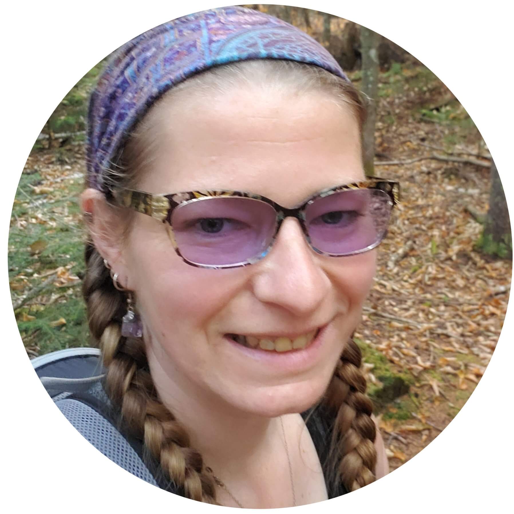 Smiling person with braids, sunglasses, and colorful headband in forest