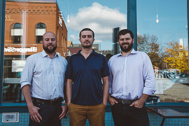 Three businessmen standing together in front of a glass storefront