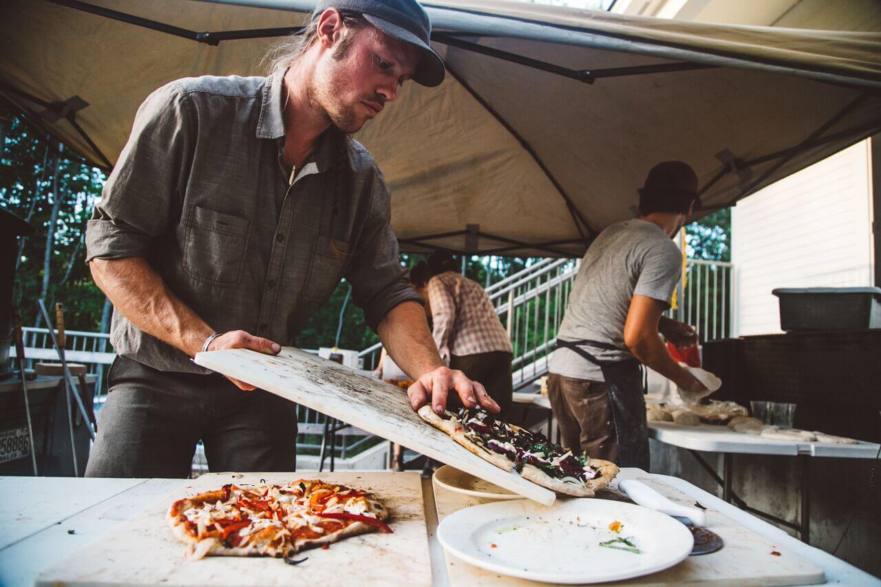 Chef preparing pizza under outdoor tent at food preparation station