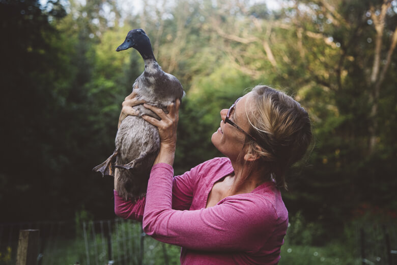Woman in pink shirt holding and looking up at a duck outdoors