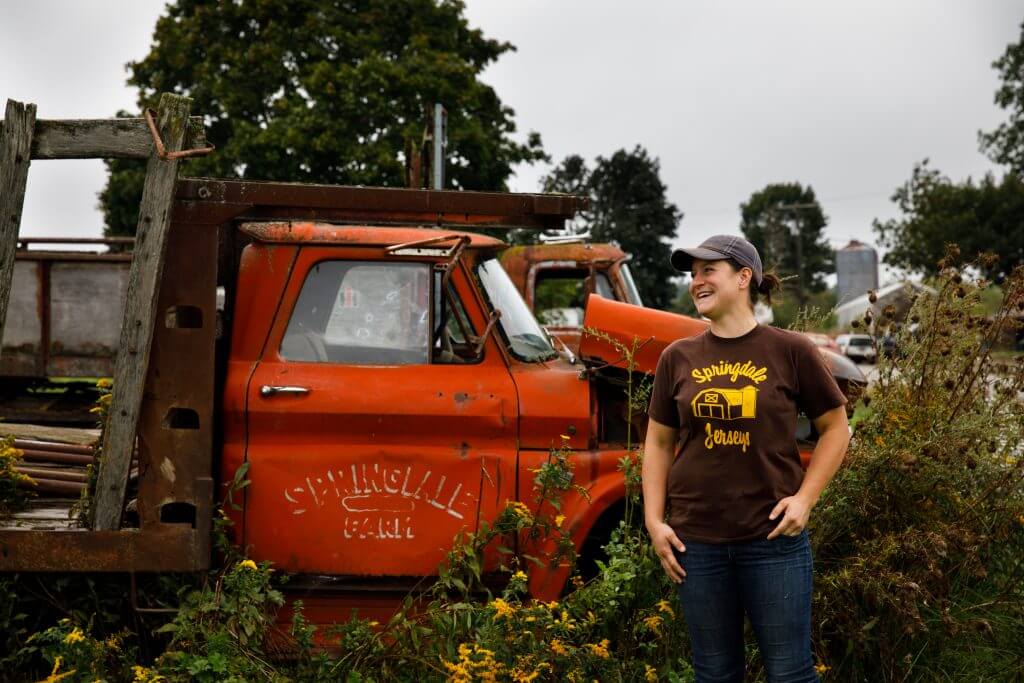 Smiling person standing next to vintage orange farm truck among yellow flowers
