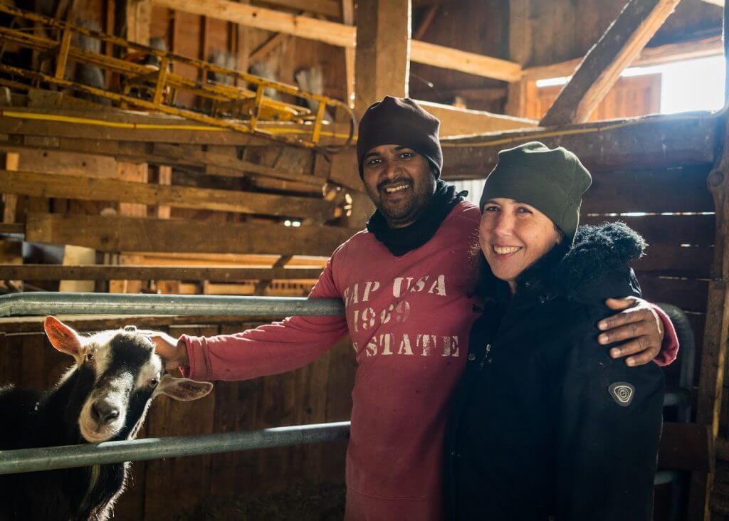 Smiling couple with goat in rustic wooden barn interior