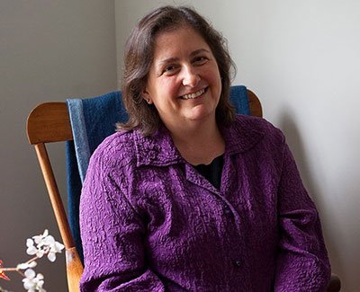 Smiling woman in purple shirt sitting in wooden chair at home