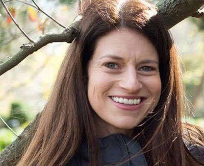 Smiling woman with long hair standing near tree branches outdoors