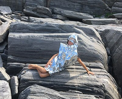 Person in blue reflective jacket reclining on layered gray rocky surface