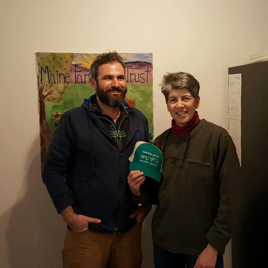 Two people standing in front of Maine Farm Trust poster