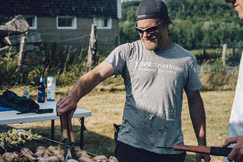 Grilling outdoors, man in triathlon shirt smiling while cooking food