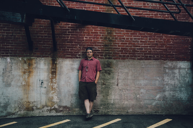 Person in red checkered shirt standing against weathered brick wall