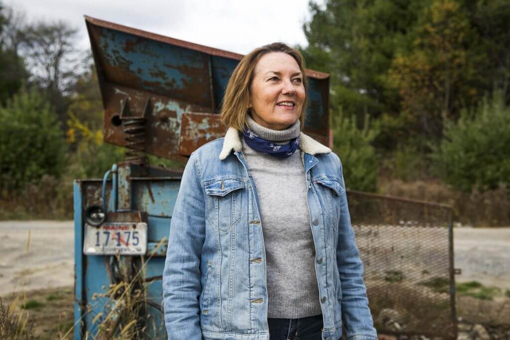 Woman in denim jacket standing near rusty blue equipment in rural setting