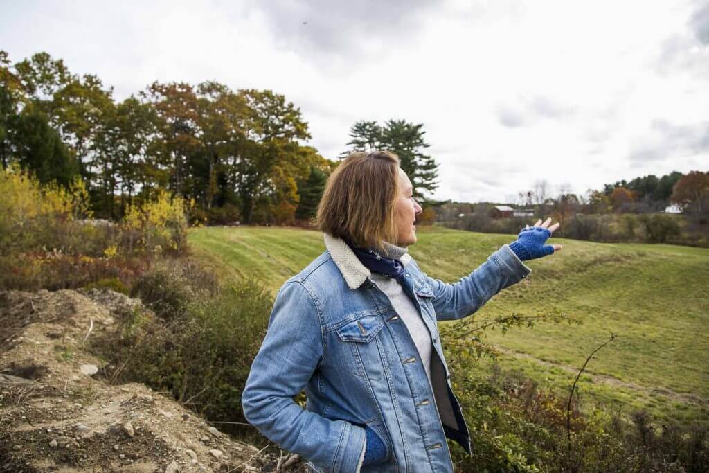 Person in denim jacket pointing across autumn landscape with trees