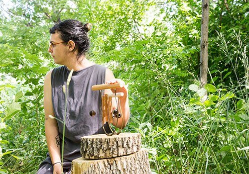 Person resting on tree stump in forest, holding wooden carving tool