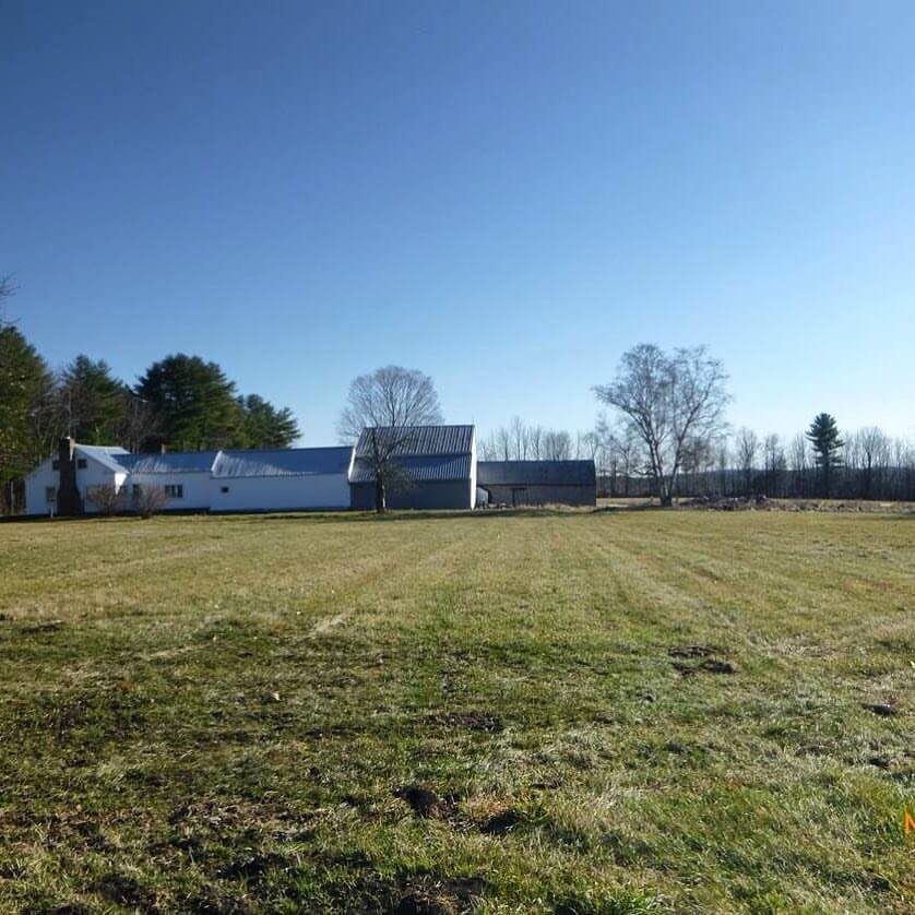 Rural farm buildings with metal roofs across open green field under clear blue sky