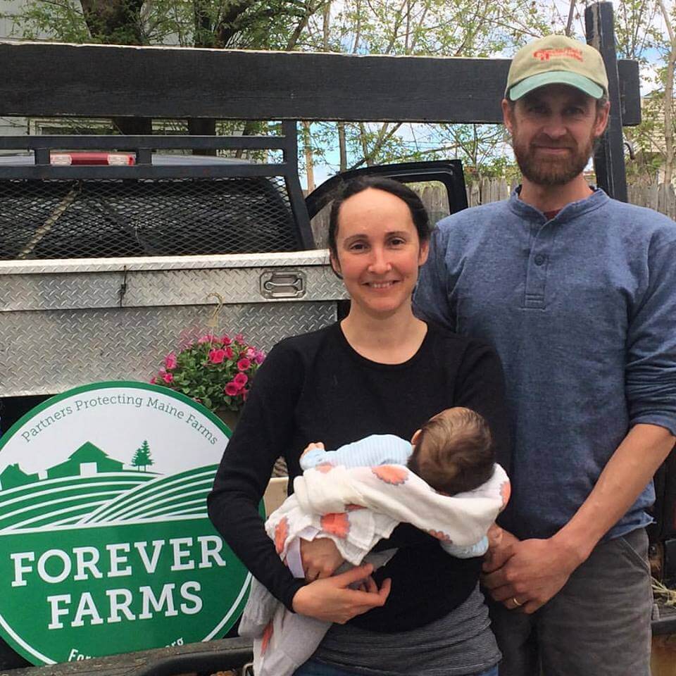 Family of three posing at Forever Farms with truck and pink flowers in background
